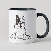A white ceramic coffee mug with a black handle and black interior, featuring a cartoon illustration of a black and white French Bulldog on the front, set against a light gray background.