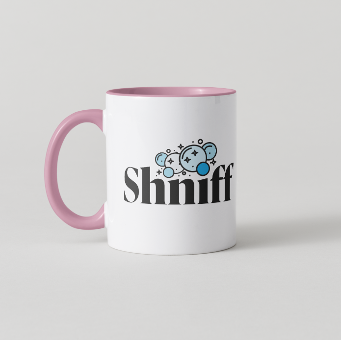 A white ceramic coffee mug with a pink handle and pink interior, featuring a black 'Shiniff' text graphic and a small blue cartoon character on the front, set against a light gray background.