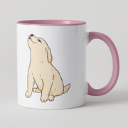 A white ceramic mug with a pink interior and handle, featuring a cartoon illustration of a light cream-colored puppy sitting and looking upward on the front.