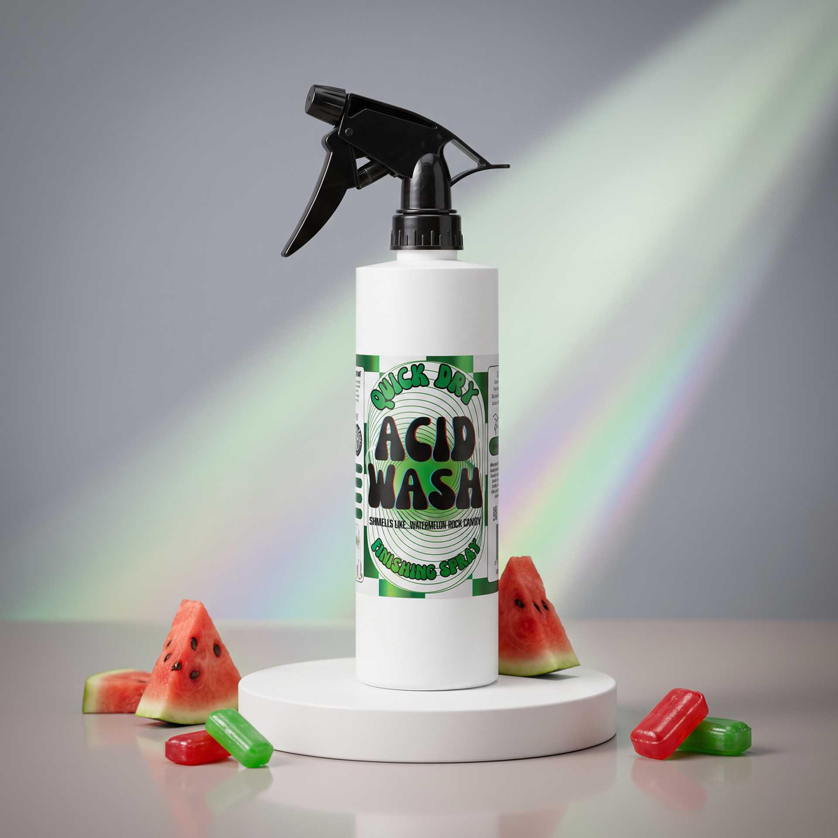 A white spray bottle labeled 'ACID WASH' with a black trigger sprayer, displayed on a white round pedestal. The bottle is surrounded by watermelon slices and red and green gummy candies on a gray surface, with soft rainbow light beams in the background.